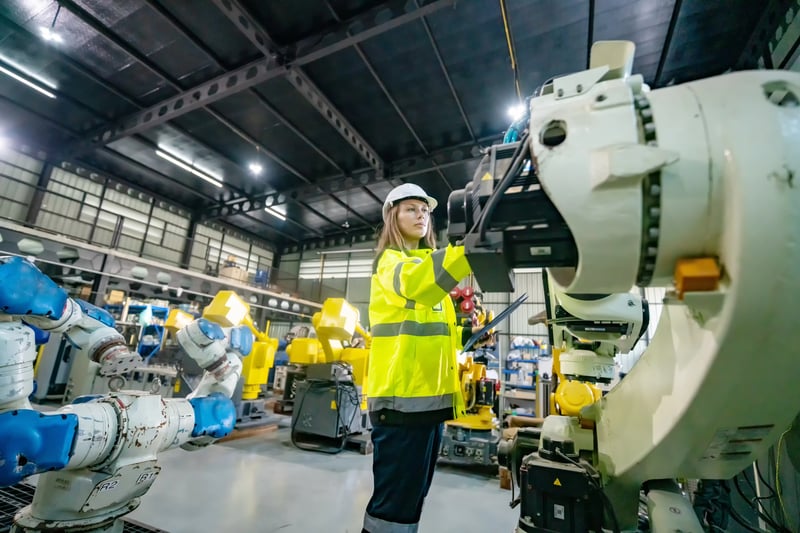 Operadora realizando manutenção autônoma em braço robótico industrial com inspeção e ajustes em ambiente fabril.