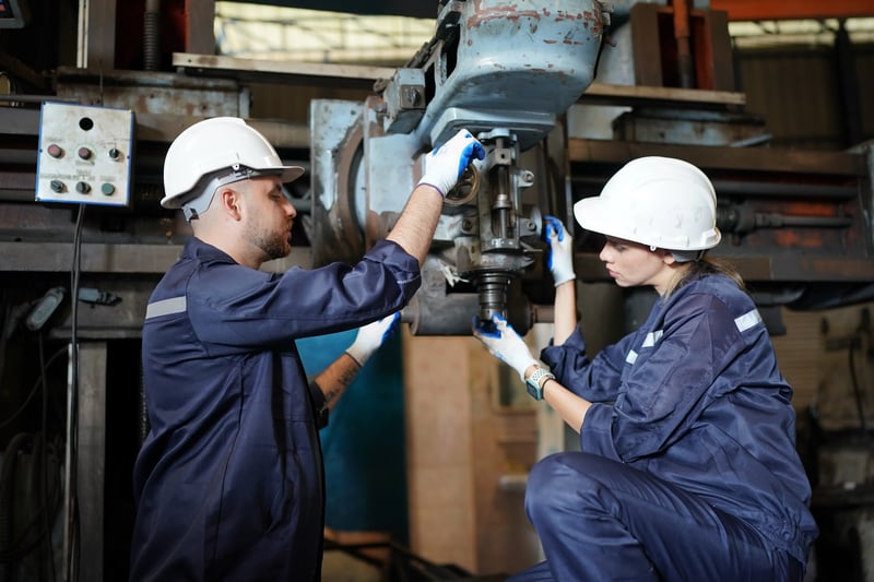 Profissionais de manutenção executando manutenção preventiva em máquina industrial, com uso de EPIs e inspeção técnica de componentes mecânicos.