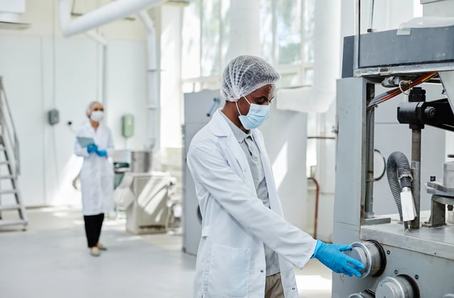 Operador de fábrica ajustando máquina industrial enquanto equipe realiza inspeção em ambiente de produção.