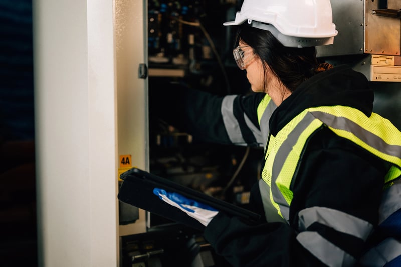Engenheira utiliza controlador para verificar máquina em auditoria de manutenção industrial.
