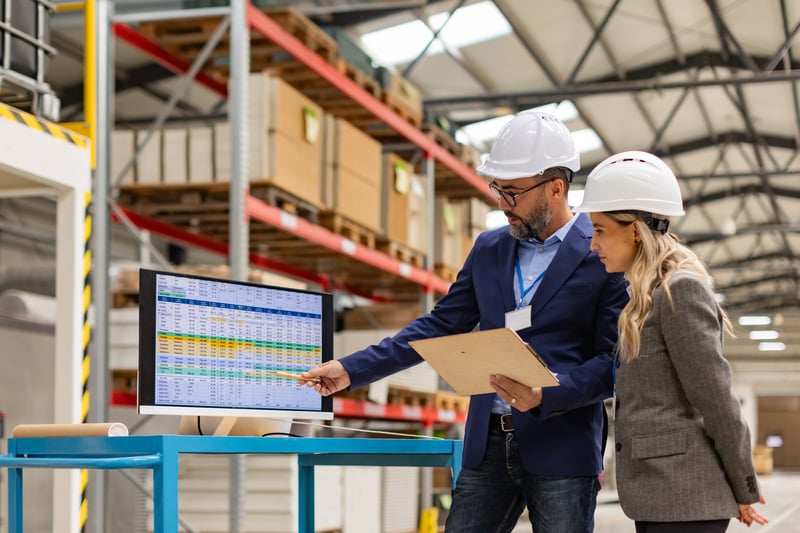 Engenheira e gerente de projetos consultam dados de manutenção em um sistema CMMS ERP na fábrica.