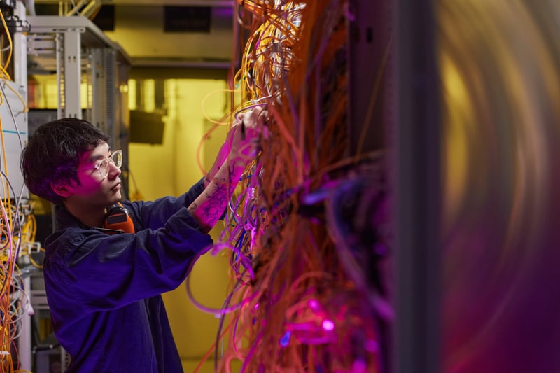 Jovem técnico conectando cabos durante a manutenção de data center em uma sala de servidores.