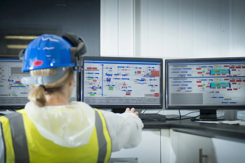 Operadora acompanhando telas de controle em central industrial com sistemas de monitoramento de condição e indicadores de desempenho dos ativos.