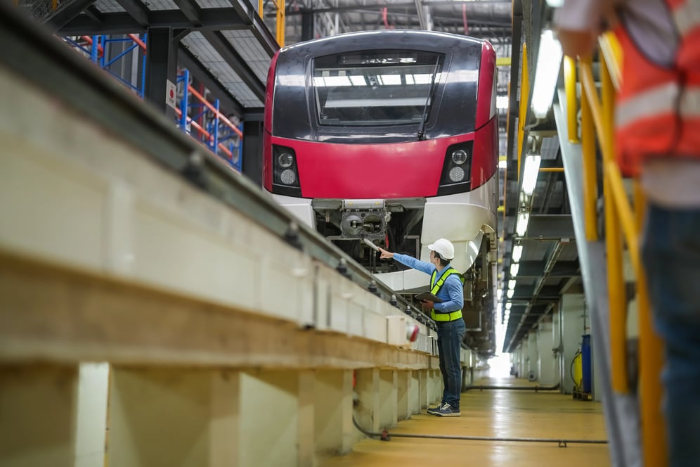 Técnico realizando manutenção preventiva em trem de transporte público dentro de oficina industrial, com inspeção de componentes mecânicos