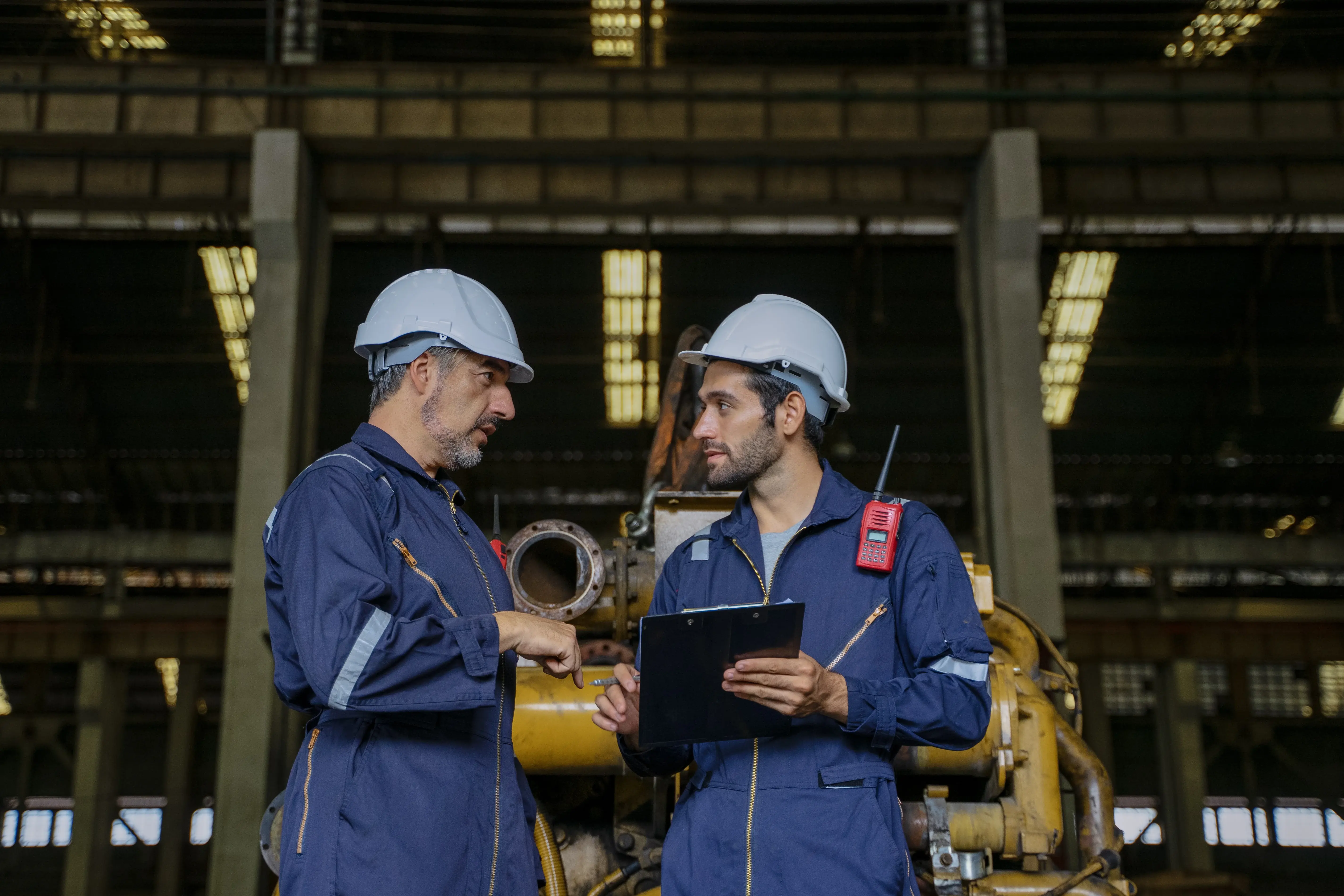 Técnicos de manutenção industrial analisando equipamento em fábrica, ilustrando a aplicação da Curva PF na gestão da manutenção e no monitoramento de falhas potenciais.