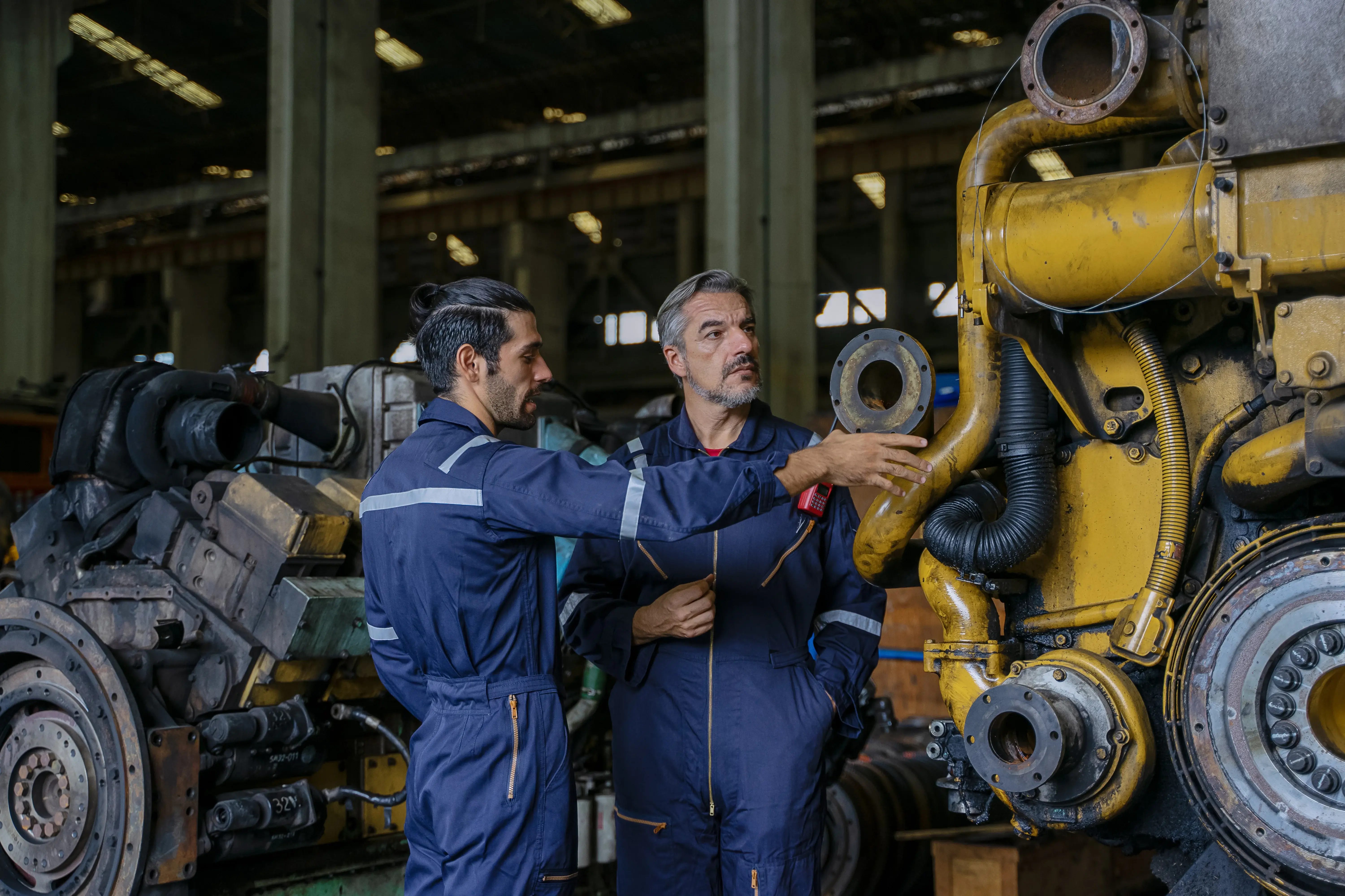 Técnicos realizando manutenção preventiva em equipamento industrial de grande porte, inspecionando componentes e conexões em ambiente fabril.
