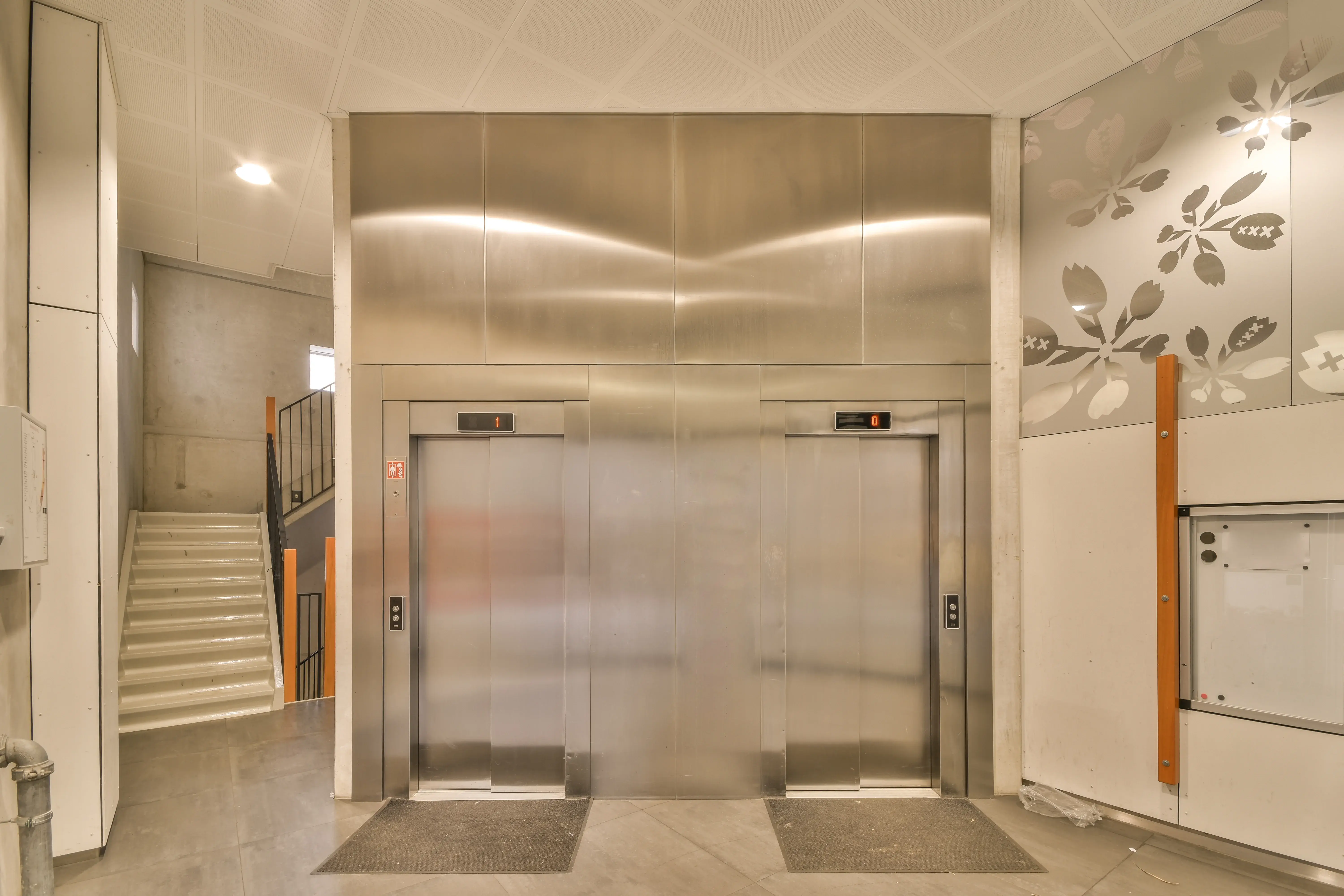 Hall de entrada de edifício com elevadores e escada, ambiente relacionado à manutenção de elevadores.