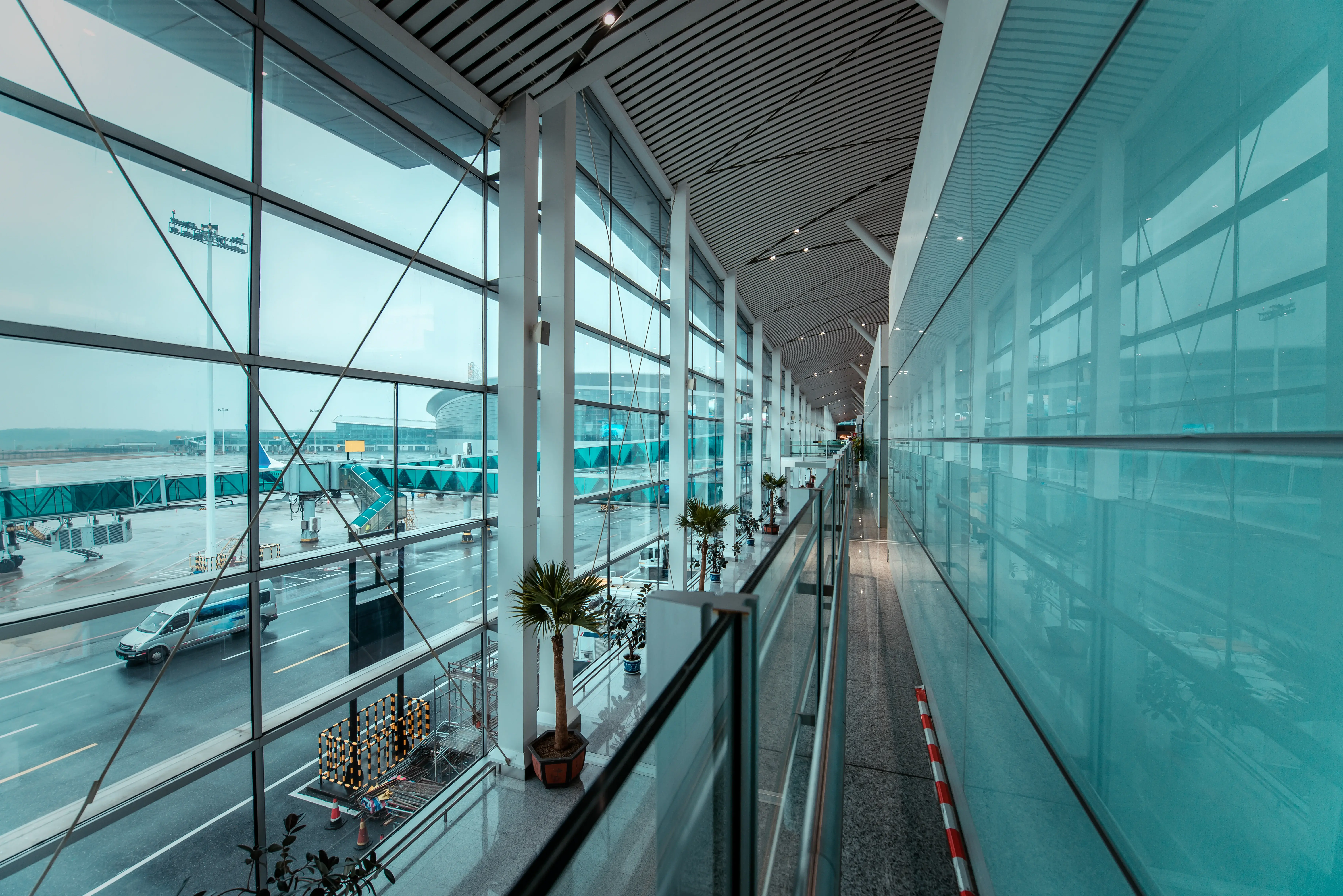 Corredor moderno de aeroporto com grandes paredes de vidro, vista para pista e pontes de embarque, destacando infraestrutura aeroportuária, mobilidade e transporte aéreo.